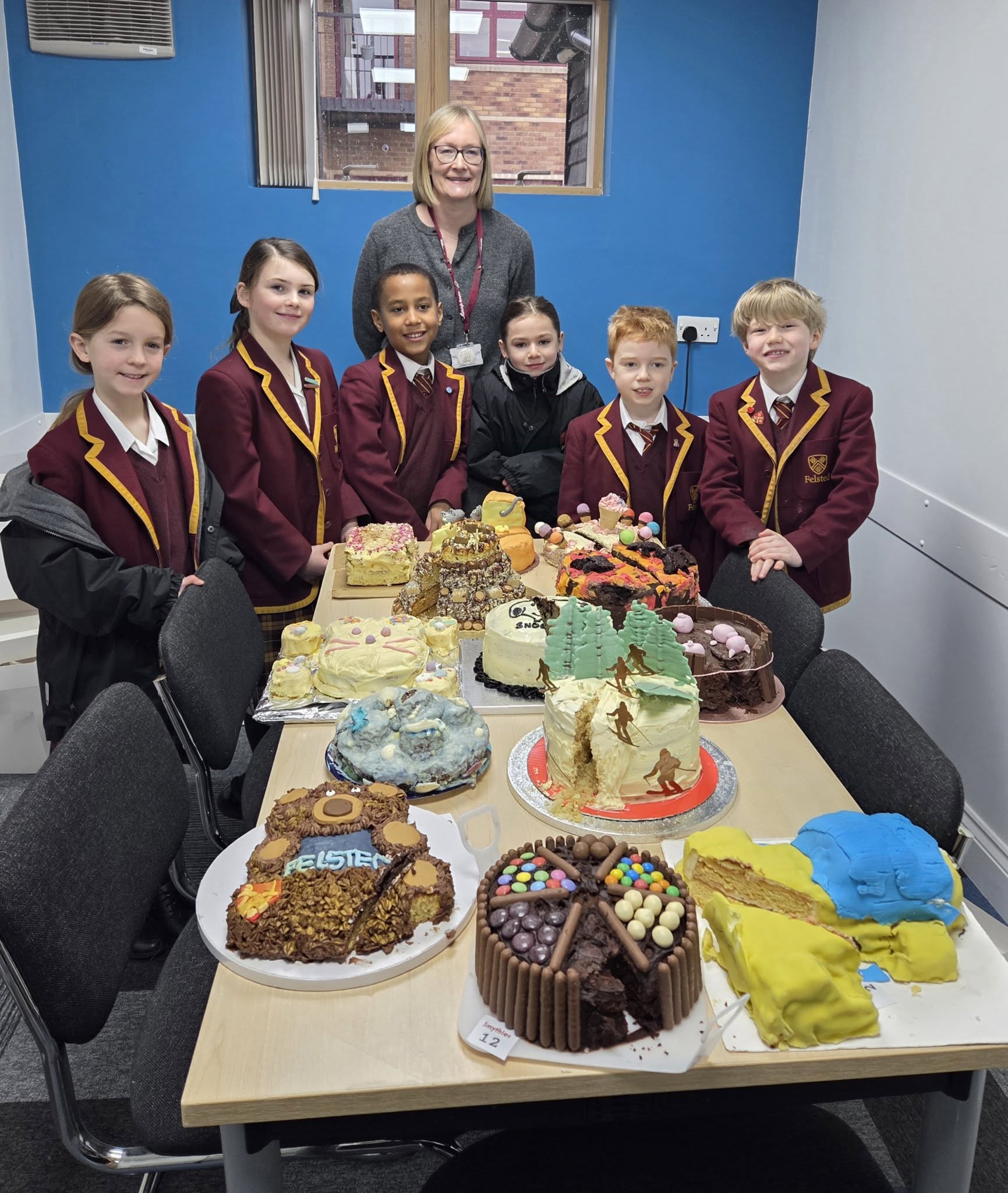 A group of school children stand around a table covered in home made cakes