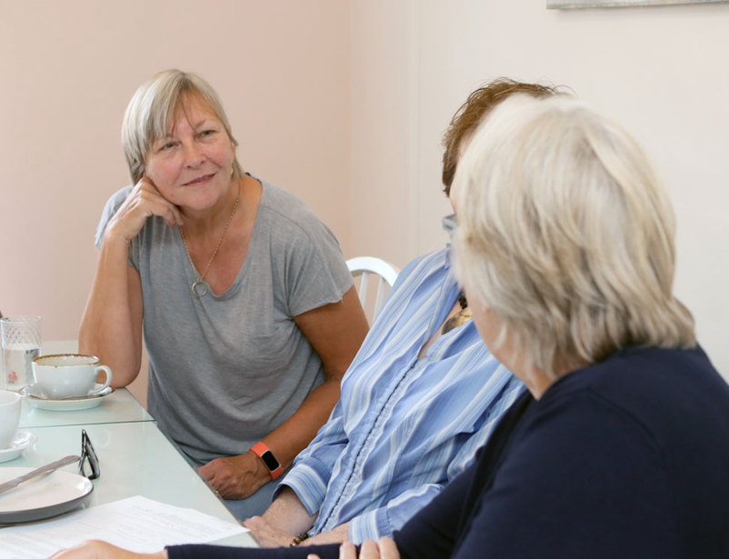 Three women sitting together at a Farleigh Hospice bereavement help point, talking over tea.
