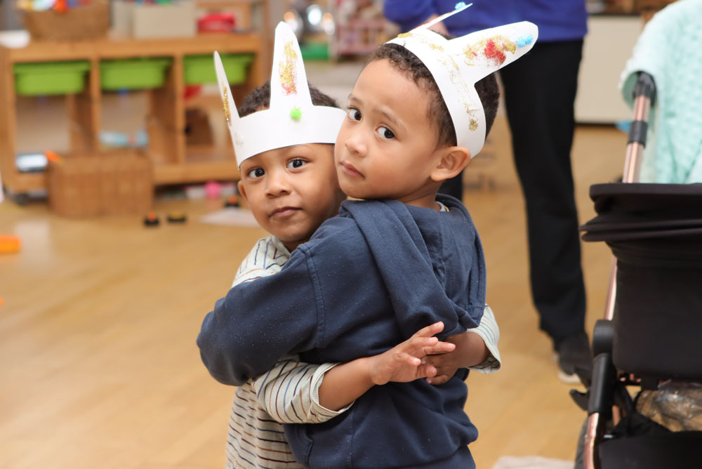 Two brothers both under 5 hugs each other while wearing home made decorated paper rabbit ears