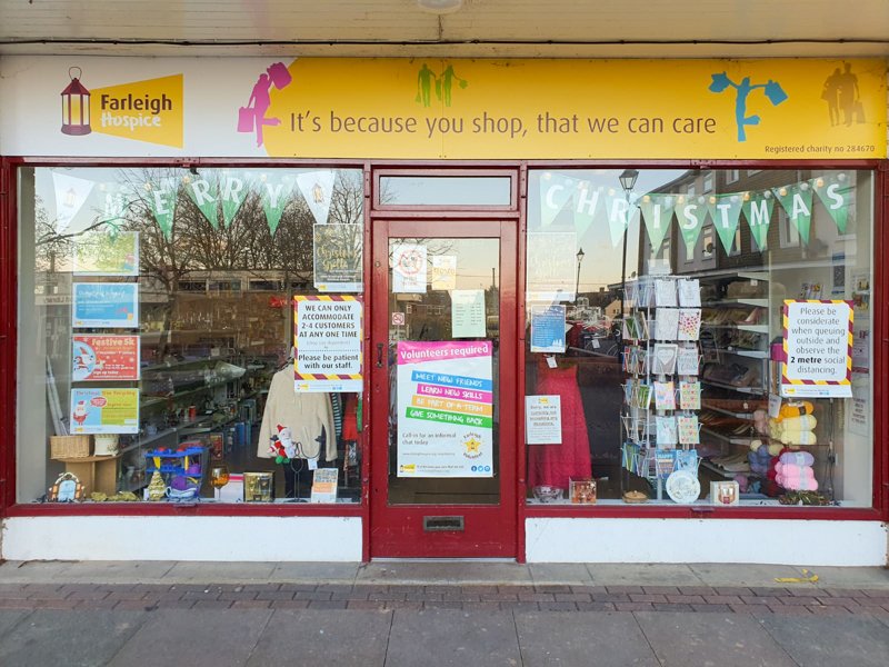 Front view of Farleigh Hospice charity shop showcasing clothing and donation information, promoting community support and charity.