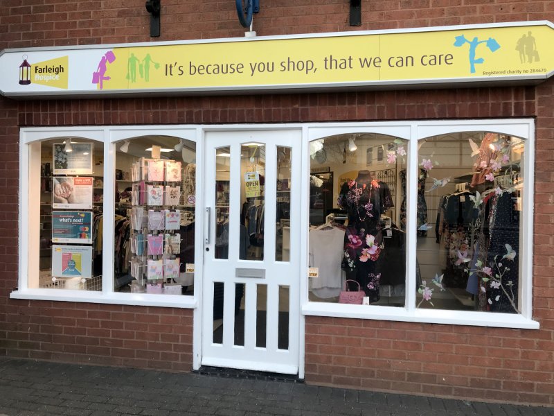Front view of Farleigh Hospice charity shop showcasing clothing displays and a welcoming sign promoting community support.