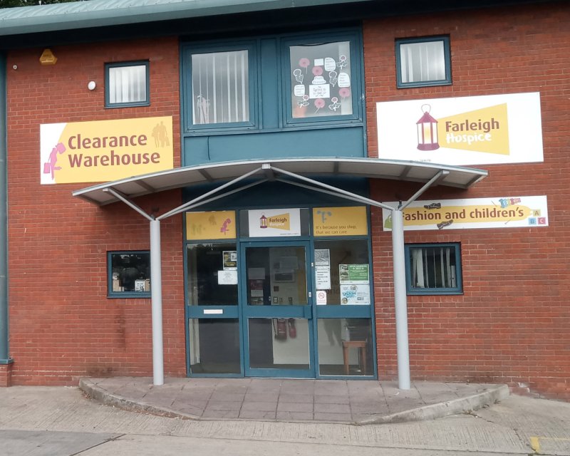 Entrance of the Clearance Warehouse featuring signage for Farleigh Hospice and children's fashion, located in a brick building.