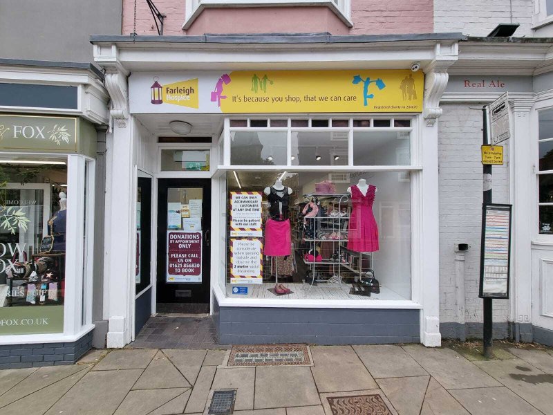 Front view of Farleigh Hospice shop showcasing vibrant pink clothing and donation information, promoting community support and charity.