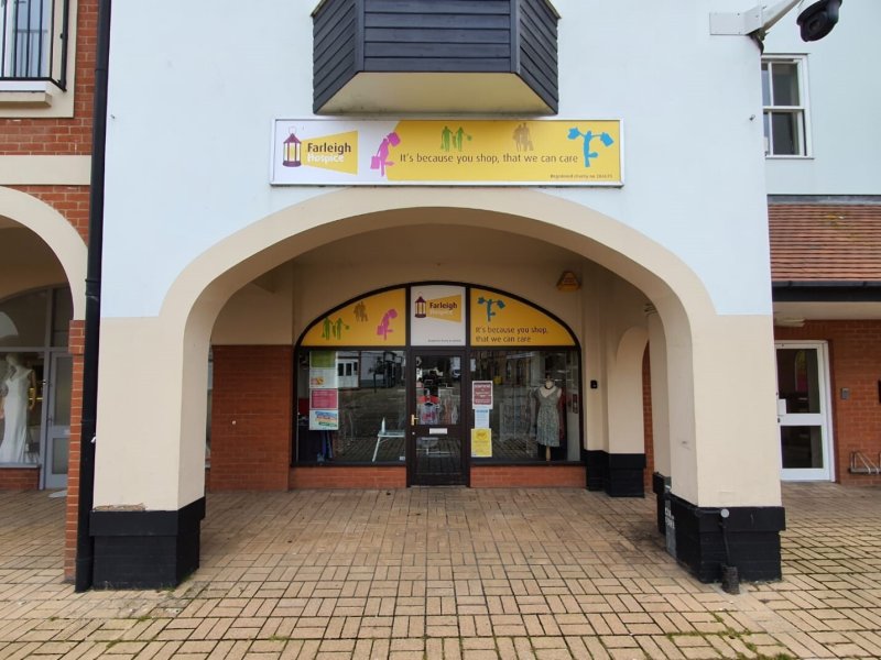 Front entrance of Farleigh Hospice shop with arched walkway and glass doors displaying various signs and mannequins inside.