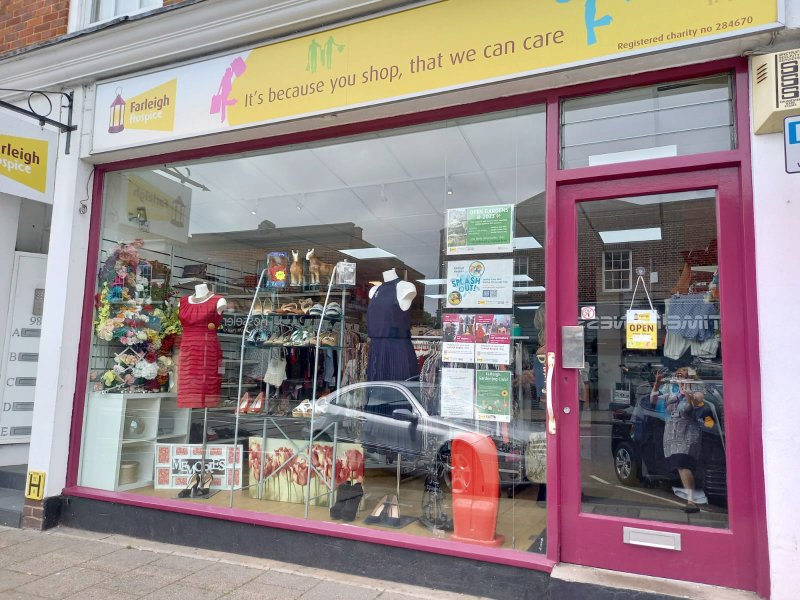 Shopfront of Farleigh Hospice charity store displaying mannequins in dresses, shoes, and various items behind a glass window.