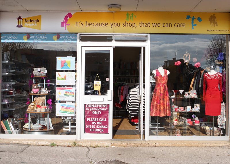 Front view of Farleigh Hospice charity shop with clothes, teddy bears, and donation signs in the window.