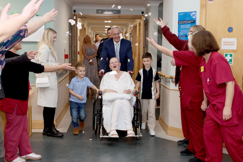 A patient is pushed in a wheelchair by her new husband after getting married at Farleigh. Nurses and family throw confetti over them.