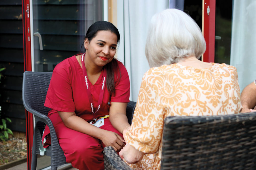 A female nurse chats to a female patient in a seated garden area outside the Inpatient Unit