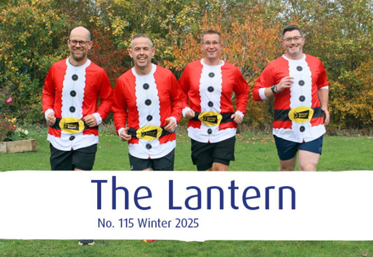Four people wearing Santa-themed tops and black shorts run outdoors in front of autumn trees, with 
