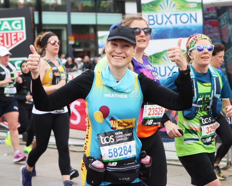 A smiling female marathon runner in Farleigh branded top gives the thumbs up to supporters