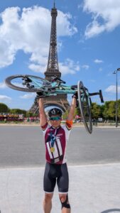 Gary in bicycle gear holding his bicycle over his head smiling in front of the Eiffel Tower.