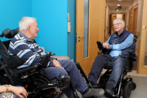 Two men both in electric wheelchairs, facing each other, chat at a Peer Support Group at Farleigh Hospice.