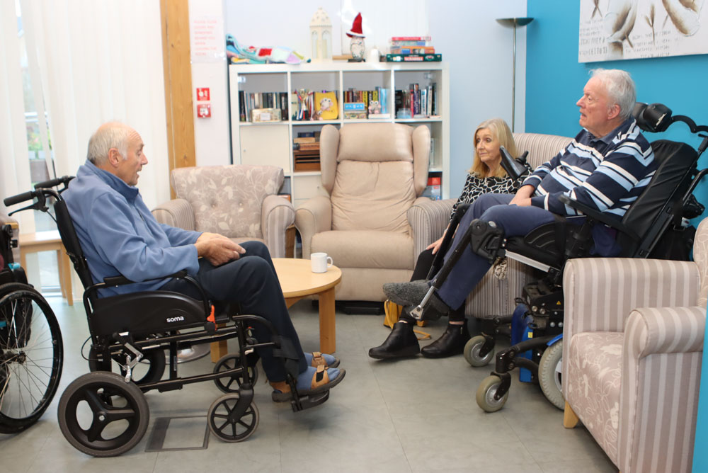 Two men both in electric wheelchairs, facing each other, chat at a Peer Support Group at Farleigh Hospice.