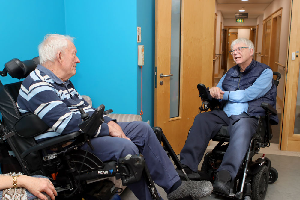 Two men both in electric wheelchairs, facing each other, chat at a Peer Support Group at Farleigh Hospice.