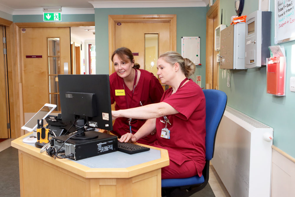 Two female nurses look at a computer screen at the reception desk of the Inpatient Unit