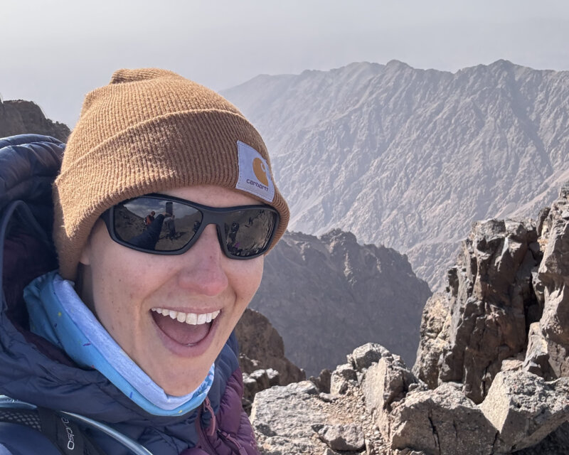 Farleigh Hospice supporter on a mountain trek, standing with scenic peaks behind her.