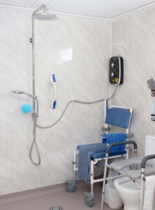 A bathroom with a shower, grab bars, a commode, and a shower chair.