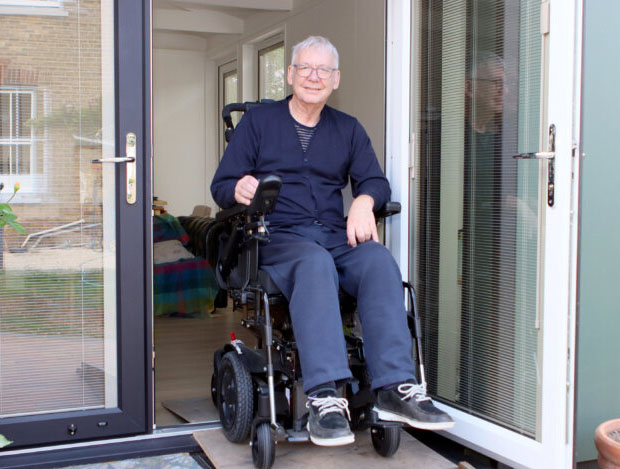 Richard, wearing dark blue t-shirt and trousers sitting in his wheelchair in the door frame to his garden annexe