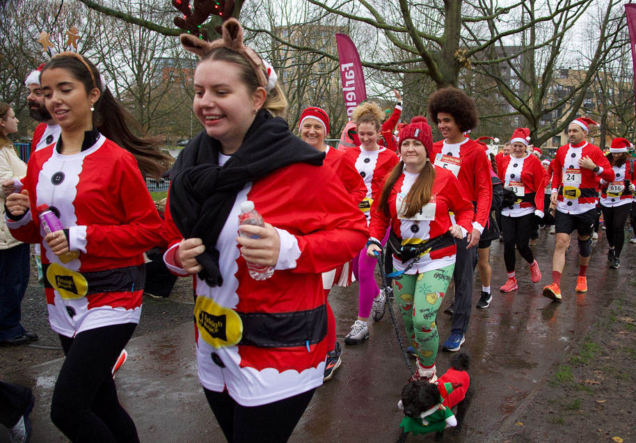 Runners in Santa-themed outfits and festive accessories participate in a 5k Christmas themed park path.