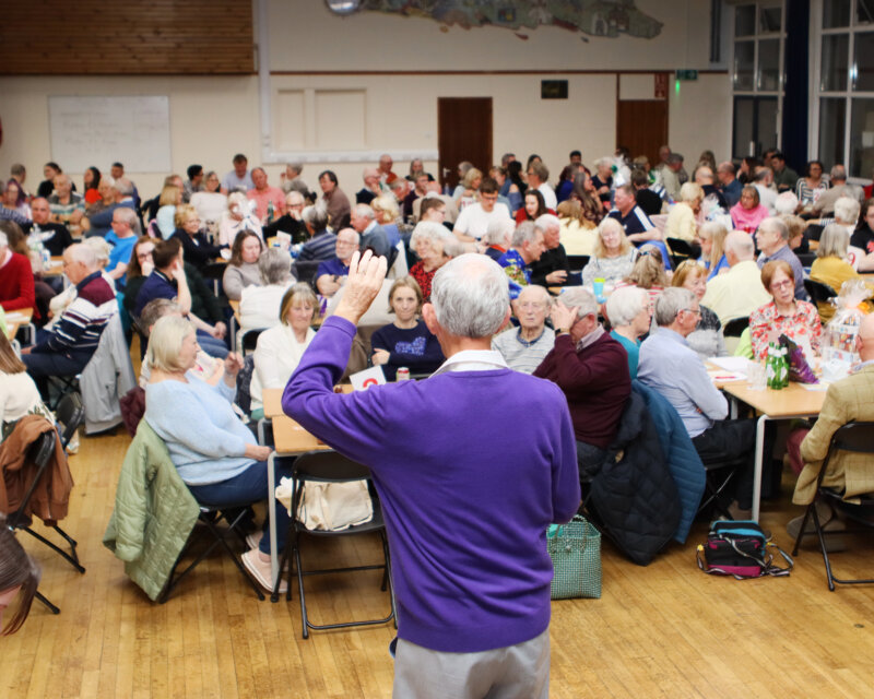 Quizmaster Chris with his back to the camera addresses 150 participants in a school hall