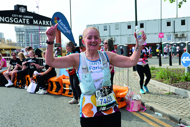 Female runner Tanya Smith holds her arms in the air as she celebrates reaching mile 19 in the 2026 London Marathon.