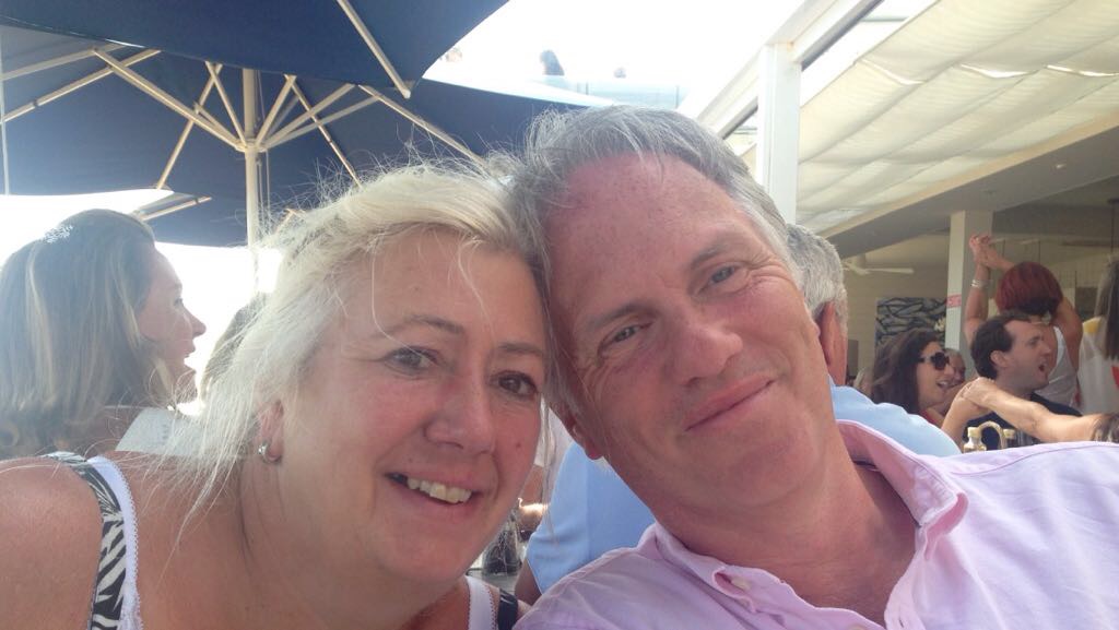 Marina, a Farleigh Hospice patient, sits with her husband Barry at an outdoor café. They’re close together in a busy, sunny setting.