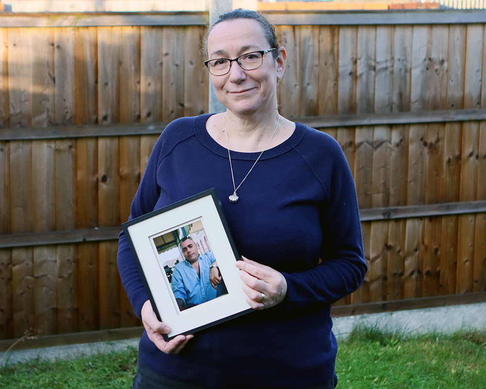 Karen Mercer, a Farleigh Hospice volunteer, standing in a garden holding a framed photo of her late husband, Lauri.