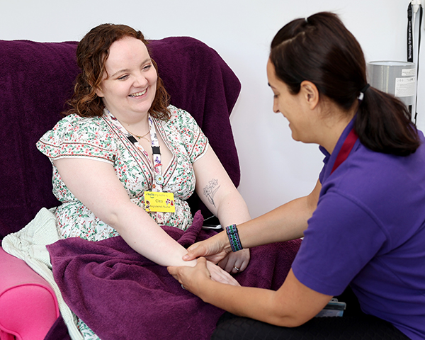 A female nurse sit in a chair and receives a hand and arm massage from a female complementary therapist