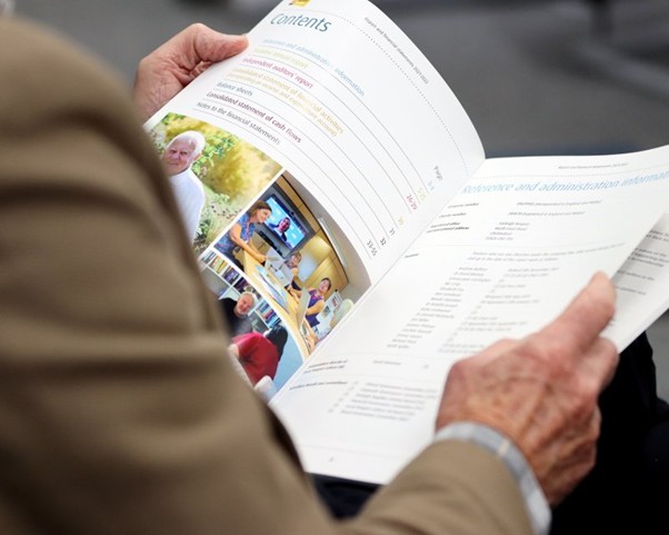 A person holds a printed booklet open to a contents page and governance information, as part of reviewing organisational materials for strategic planning.
