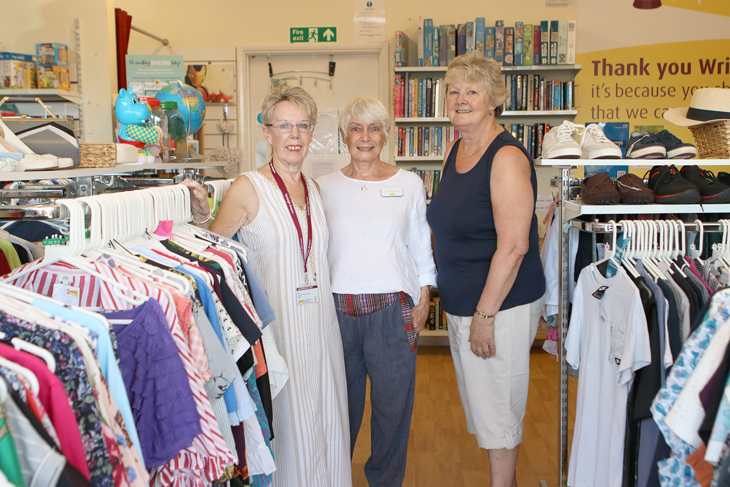 Three women stand between the clothes rails in the Writtle Farleigh store smiling at the camera