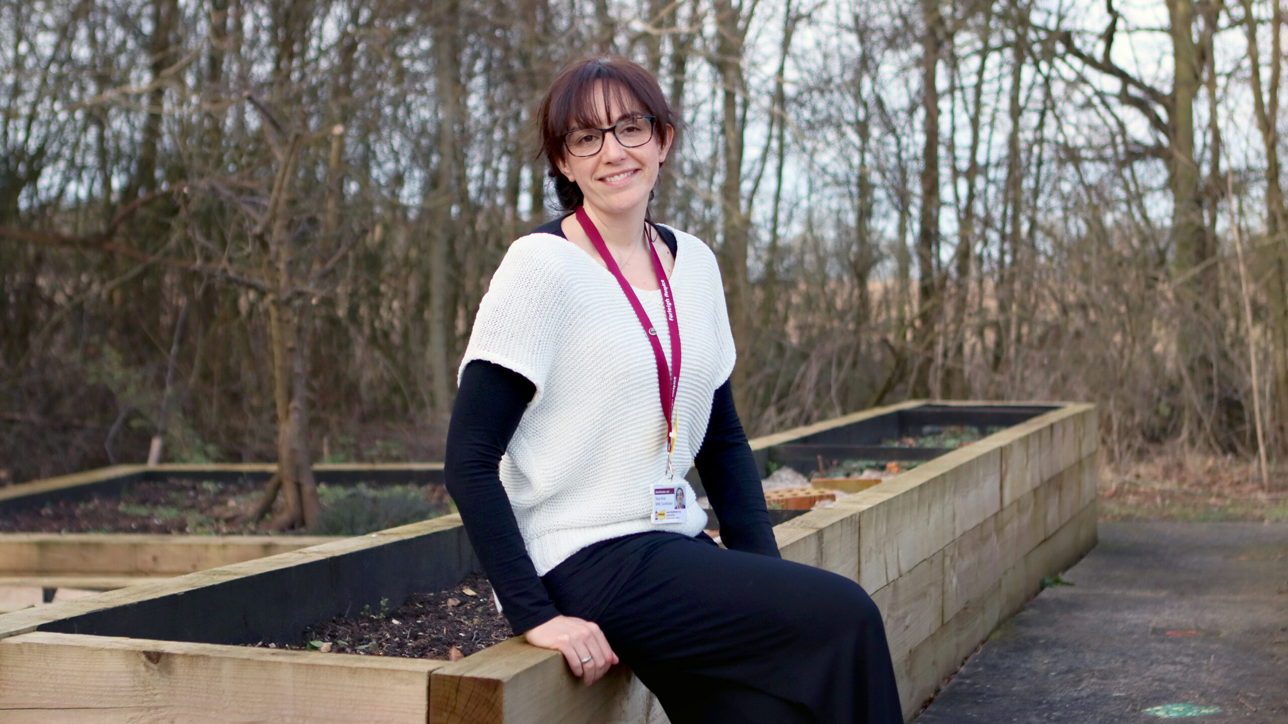 Tessa Rose, Farleigh Hospice’s Motor Neurone Disease Coordinator, sits on the edge of a raised garden bed.
