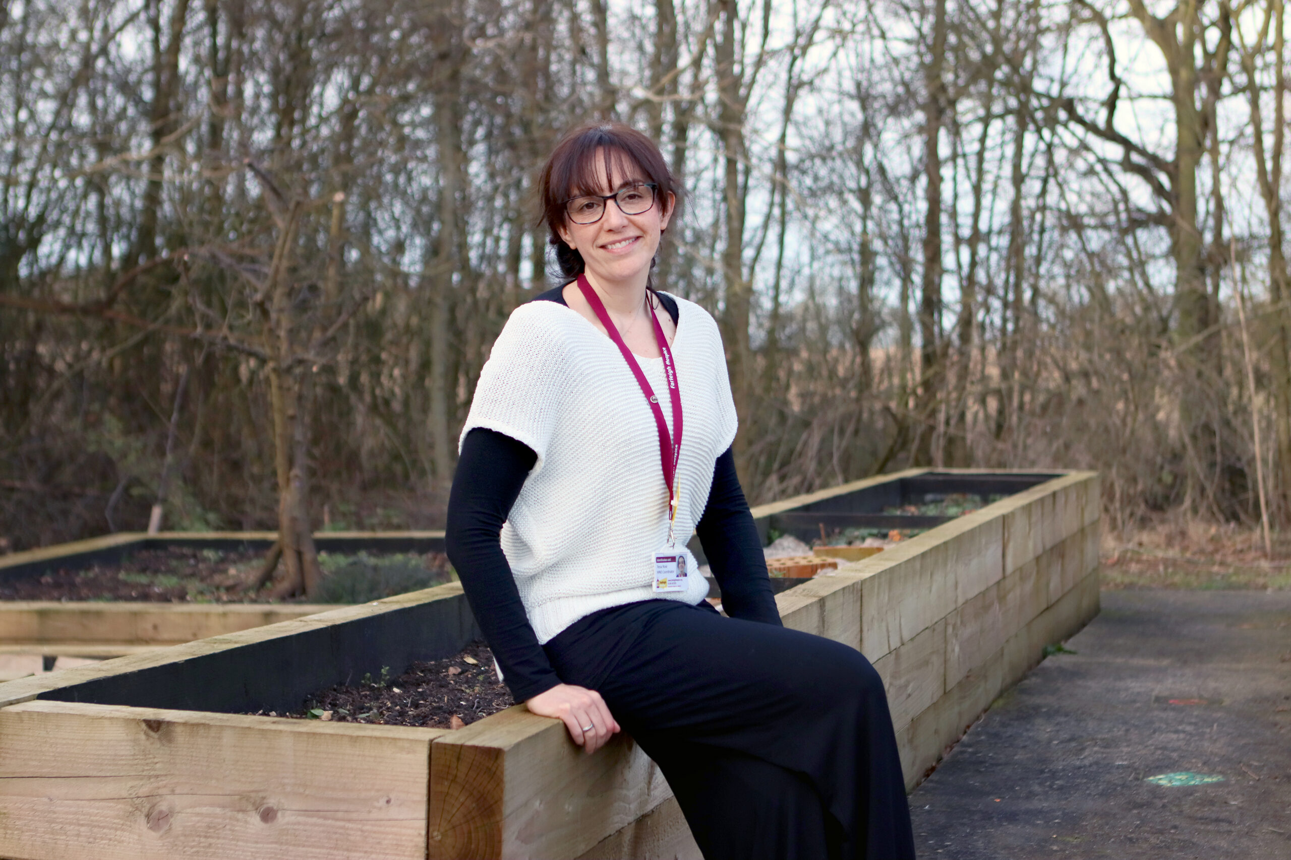 Tessa Rose, Farleigh Hospice’s Motor Neurone Disease Coordinator, sits on the edge of a raised garden bed.