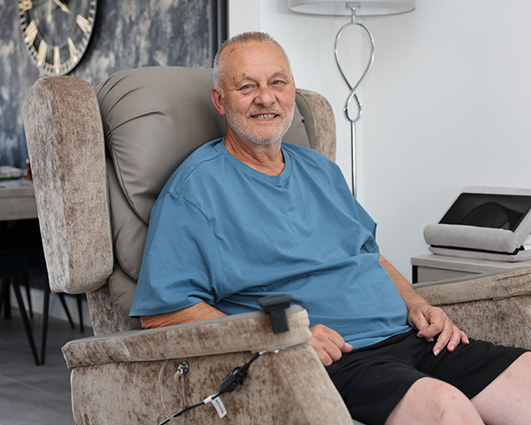 Male patient Jim seated in his armchair in his lounge at home