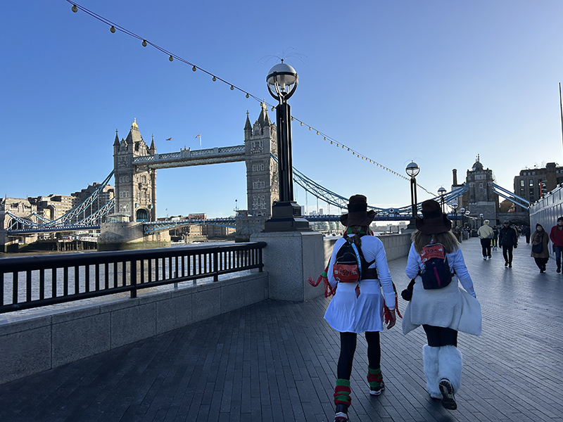 Two people taking part in a sponsored walk along the Thames path with Tower Bridge in the background in the early morning