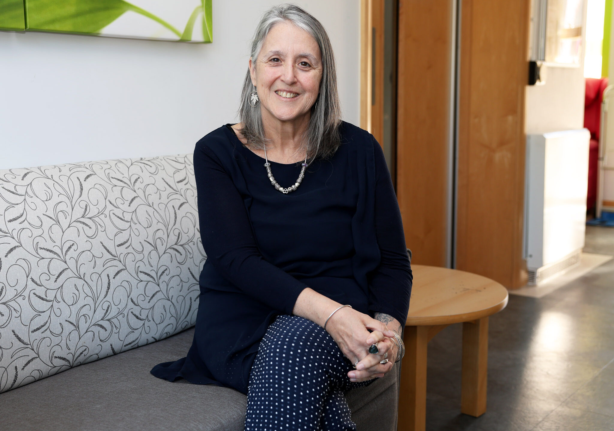 Michelle Kabia, Chief Executive of Farleigh Hospice, seated on a patterned couch in a bright, welcoming room, smiling toward the camera.