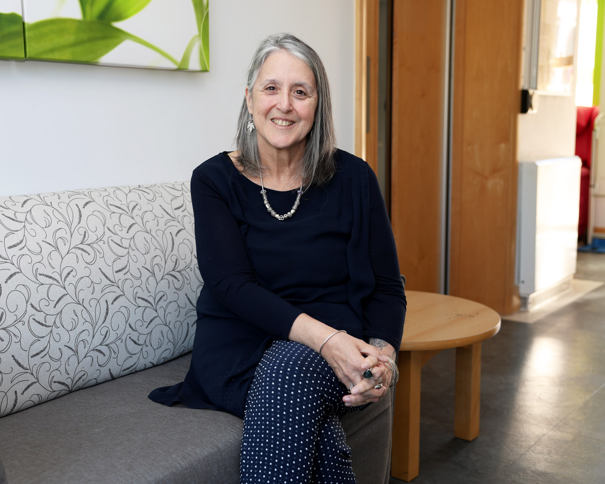 Michelle Kabia, Chief Executive of Farleigh Hospice, seated on a patterned couch in a bright, welcoming room, smiling toward the camera.